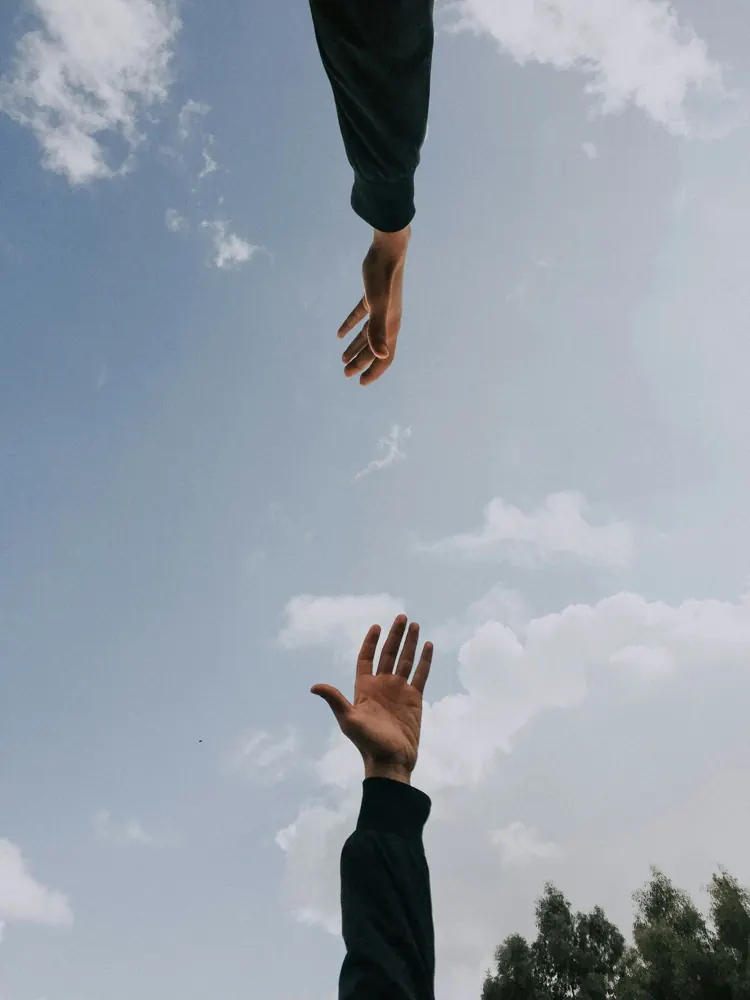 Two hands reaching towards each other against the sky