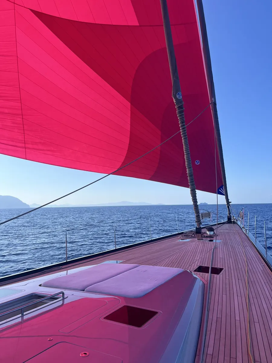 The teak deck of a sailing yacht under a red gennaker